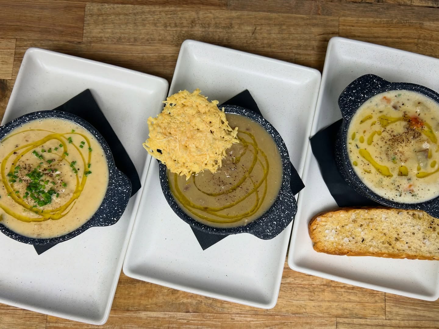 assorted soups 3 with spoons they are brown and topped with swirls of olive oil and slices of bread