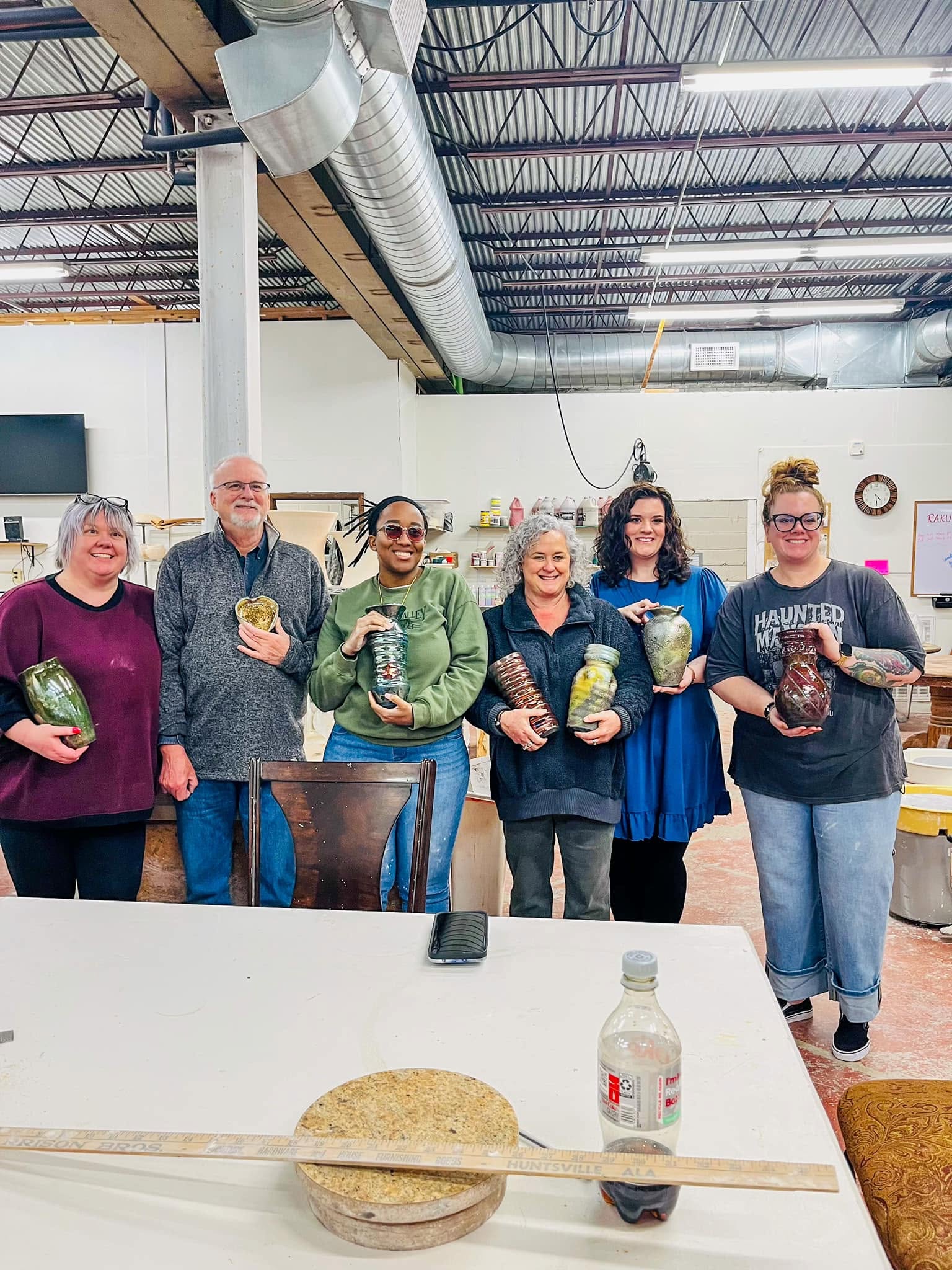 smiling group of humans with hand made pottery standing in a concrete white background space