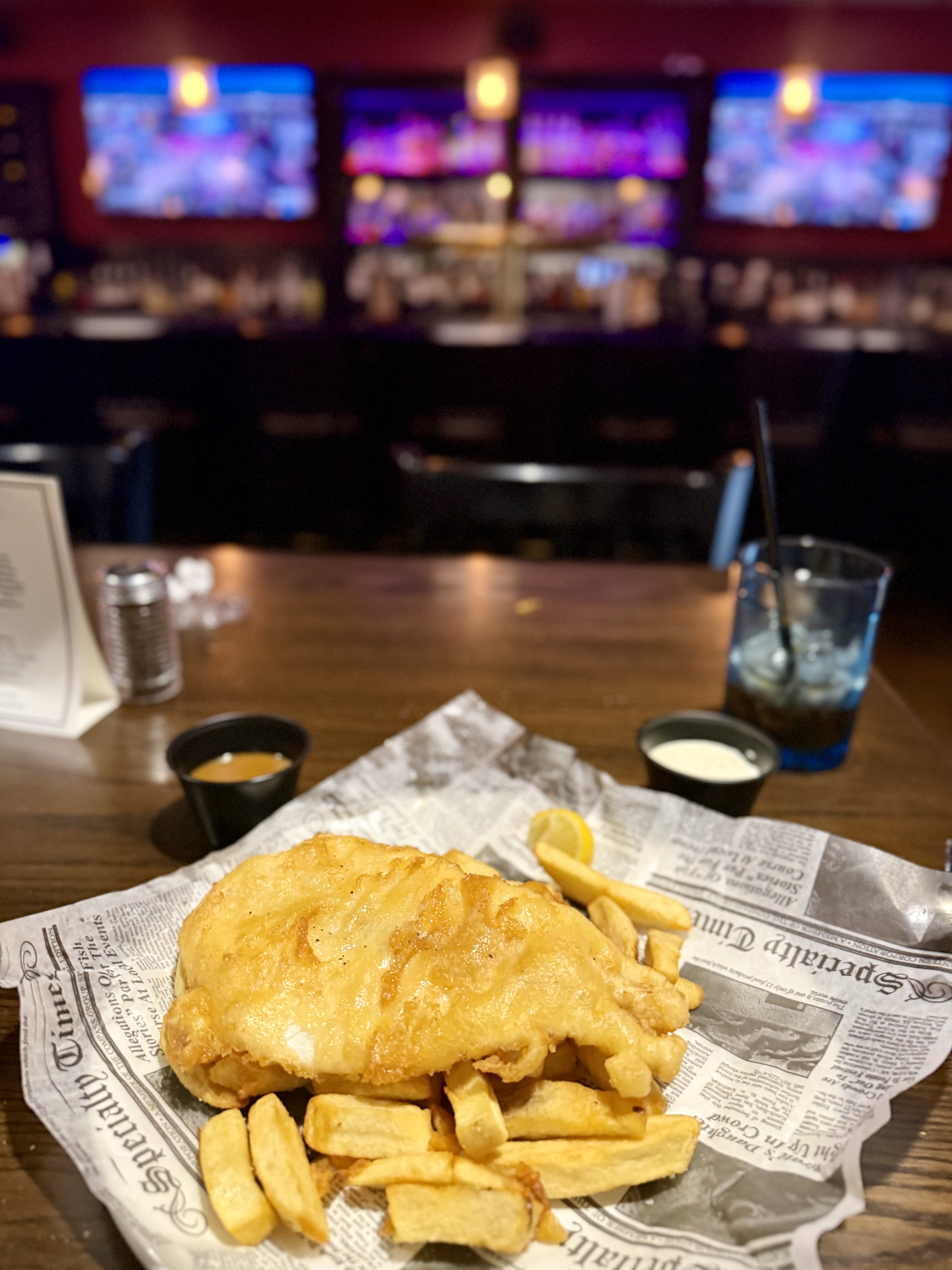 fish and chips on a platter with a lit bar behind it