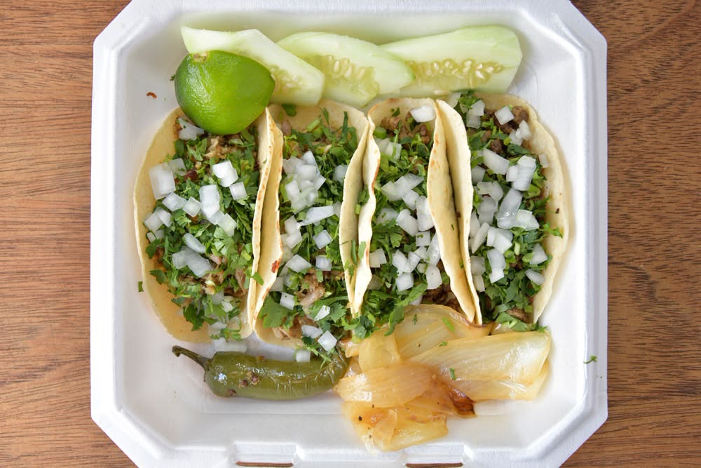 white styrofoam box of traditional tacos with onions and cilantro